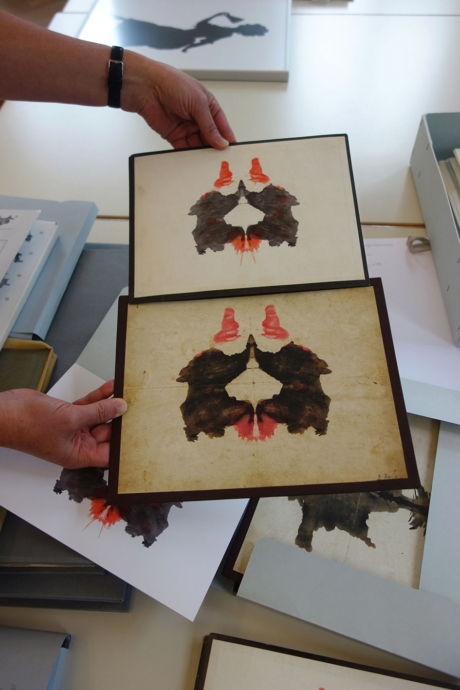 Die Archivarin zeigt zwei verschiedene Ausgaben von historischen gedruckten Flecken aus dem Rohrschach-Test